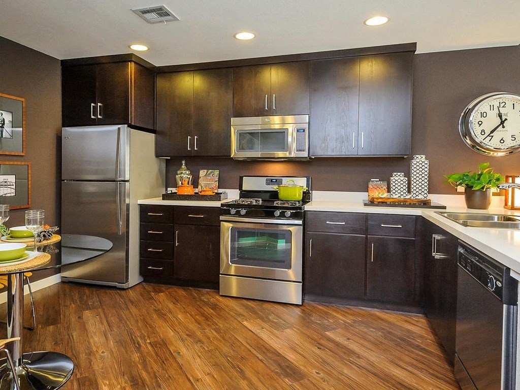 Foster City, CA Apartments - The Plaza - Kitchen with Hardwood Style Flooring, Stainless-Steel Appliances, Brown Flat-Panel Wood Cabinets, and White Stone Countertops