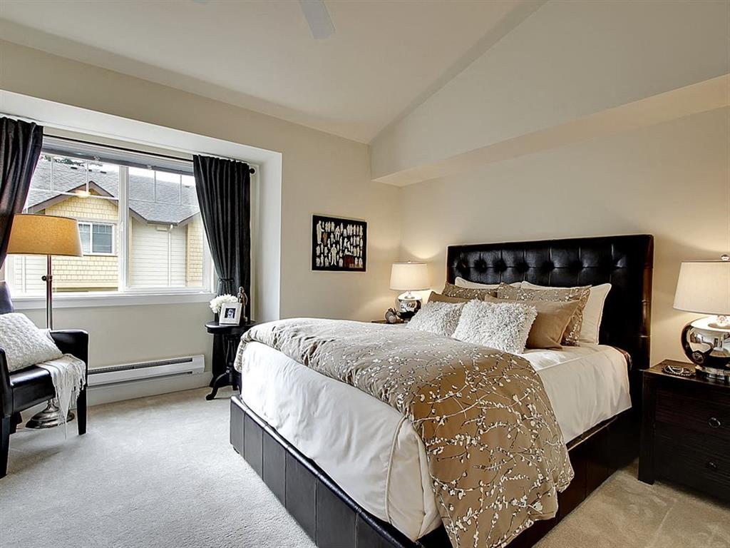 Three Bedroom Apartments in Kenmore WA - Northshore Townhomes - Furnished Bedroom with a Large Bed, Carpeted Floor, Black Nightstands with Lamps, an Armchair, Window, and Standing Lamp