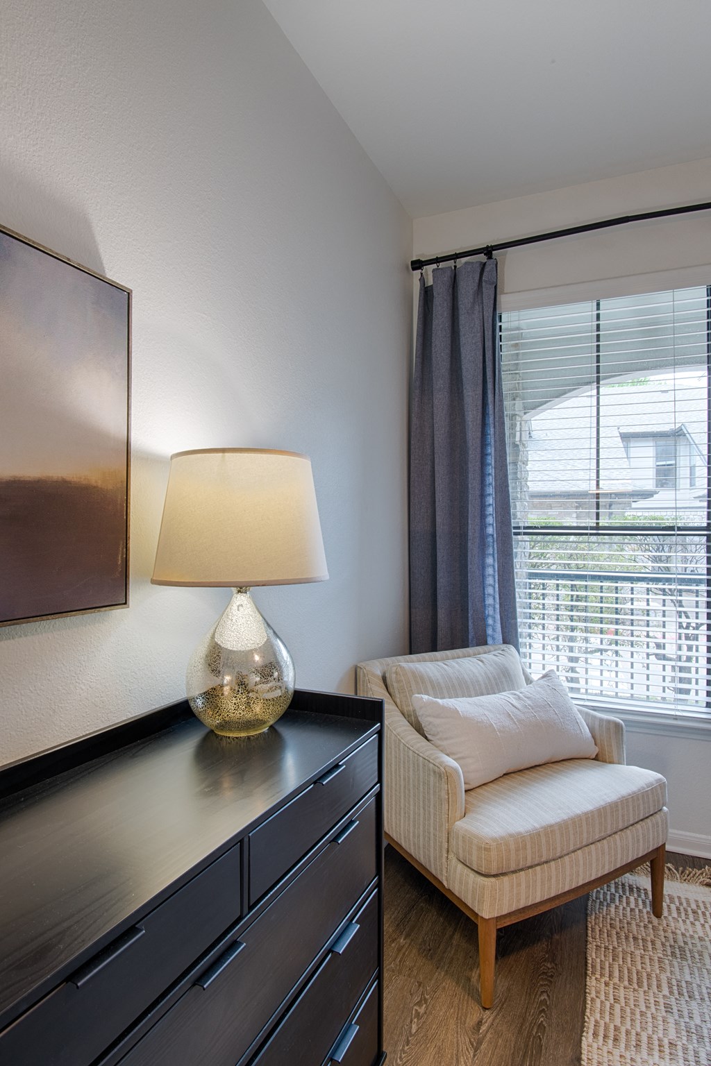 a bedroom with a chair and a dresser with a lamp on it