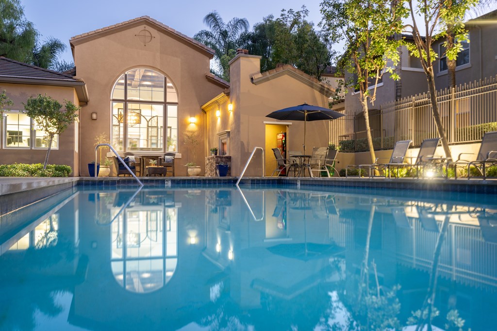 A swimming pool in a backyard with a patio and a tree.