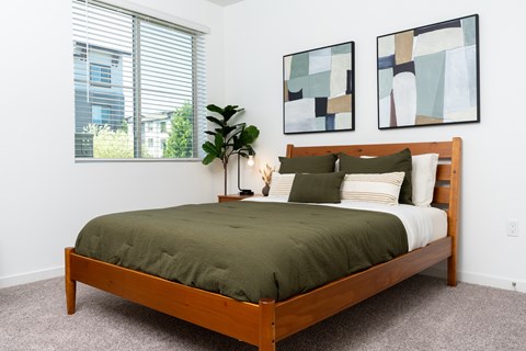 A bedroom with a bed, pillows, a plant, and two paintings on the wall.