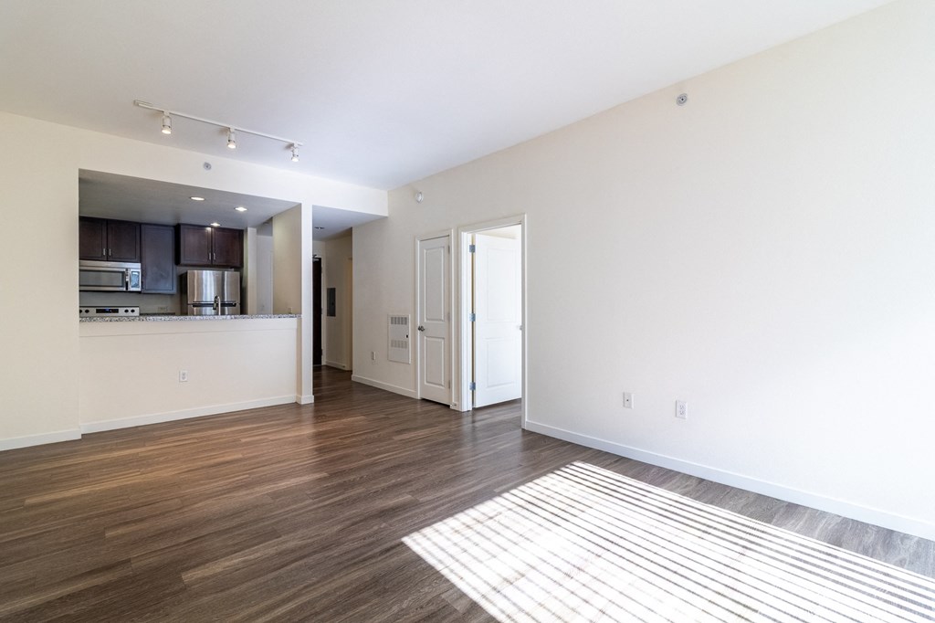 an empty living room and kitchen with wood flooring and white walls