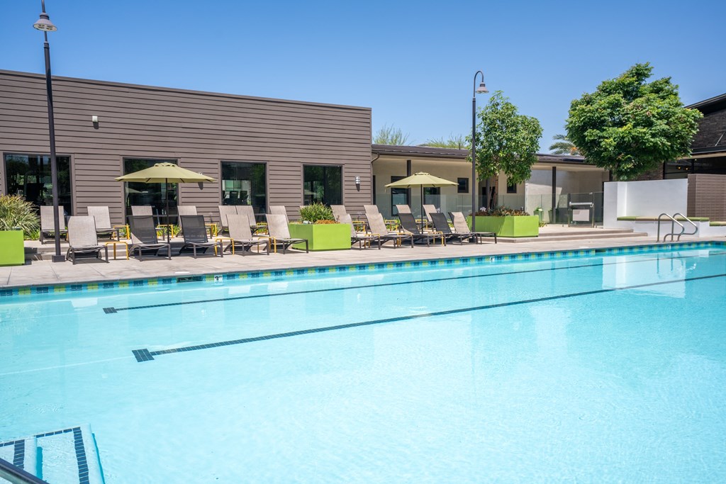 A swimming pool with sun loungers and umbrellas in front of a building.