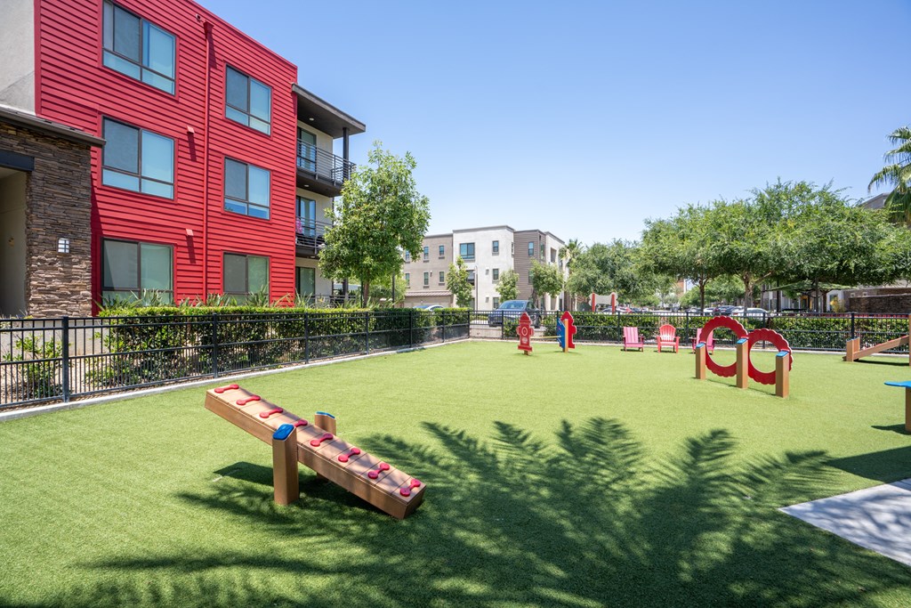 A playground with a seesaw and slides in front of a red building.