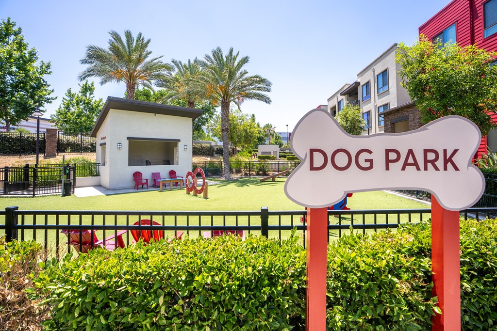 A dog park sign is in front of a building and a fence.