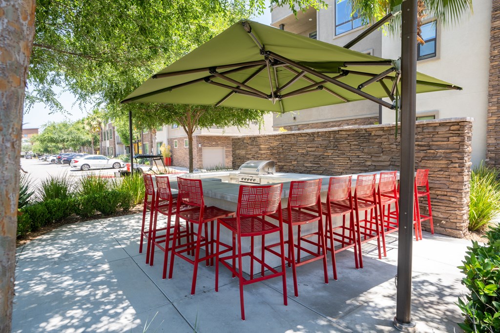 A table with red chairs is under a green umbrella.