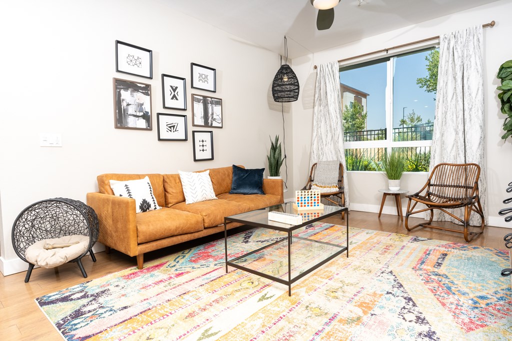 A living room with a yellow couch, a glass coffee table, and a colorful rug.