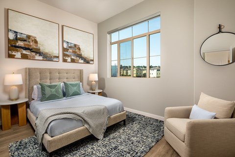 A bedroom with a large bed and a chair with window view.