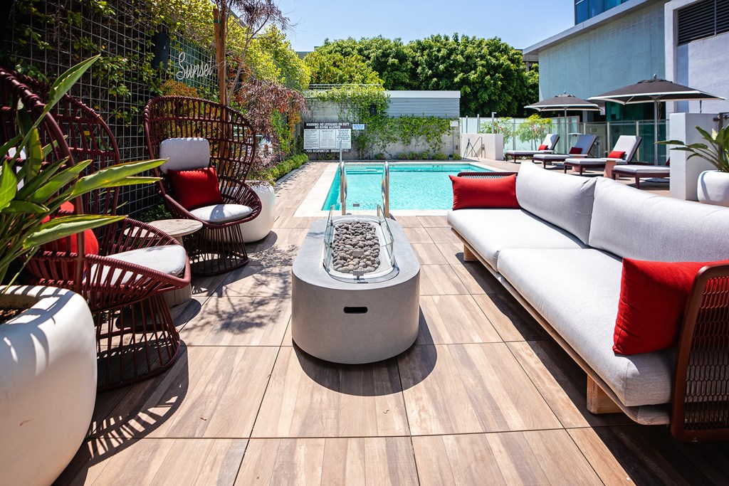 a backyard with a pool and lounge area with a white couch and red pillows