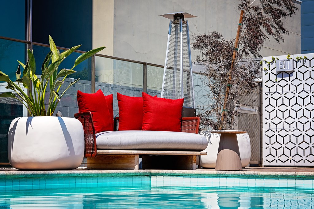 a lounge area next to a pool with a red cushion on a couch