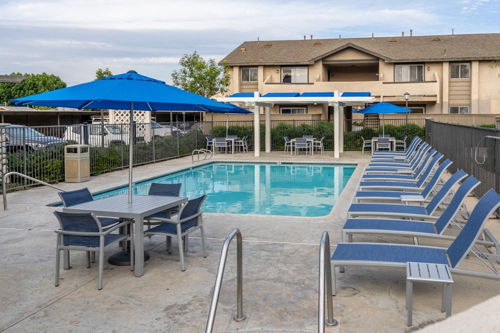 a swimming pool with blue chairs and umbrellas and a building in the background at Sunstone Place, Riverside, California