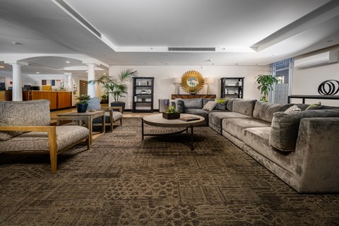 A living room with a patterned carpet and a variety of furniture including a sofa, armchair, and coffee table.