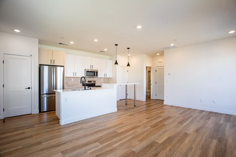 an open kitchen and living room with white cabinets and wood flooring