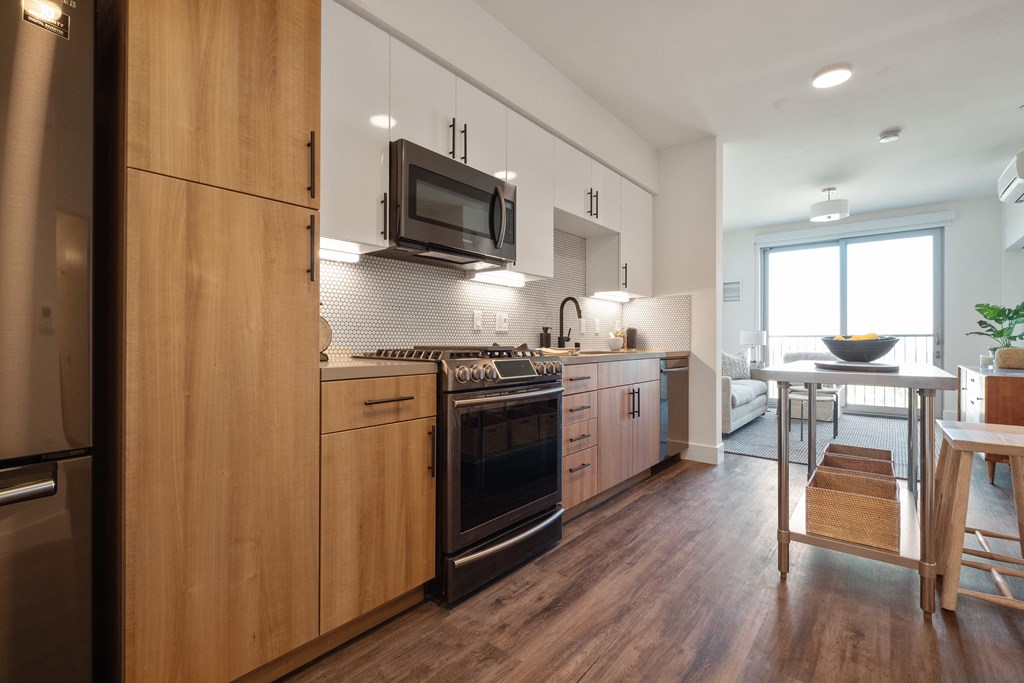 Three-BR Apartments In Downtown Berkeley, CA - The Addison - Designer Kitchen With Black Stainless Steel Appliances, 2-Color Custom Kitchen Cabinetry With Silestone Quartz Countertop and Designer Backsplashes, Hardwood Floors Leading To Living Room