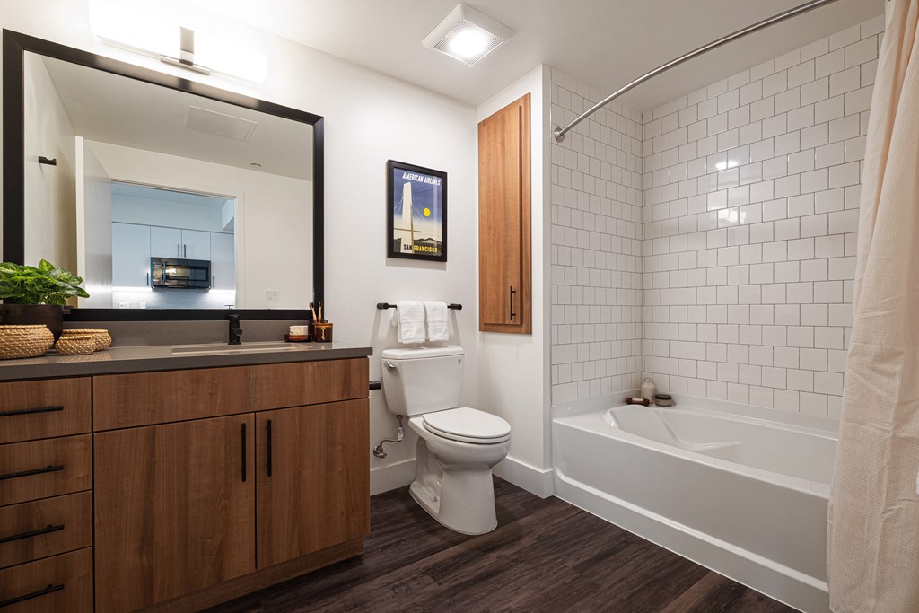 Berkeley, CA, Apartments for Rent - The Addison - Bathroom with Wood-Style Flooring, Modern Style Vanity, Wood-Tone Cabinetry, and Shower/Tub Combo with Full-Height Tile Backsplash.