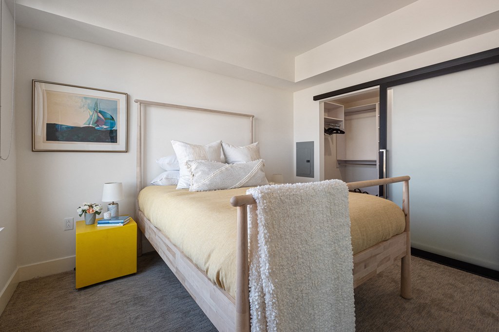 Luxury Three-Bedroom Apartments in Berkeley, CA - The Addison - Bedroom with Carpeted Flooring, Bed, Nightstand with Lamp, Framed Wall Art, and Spacious Closet.