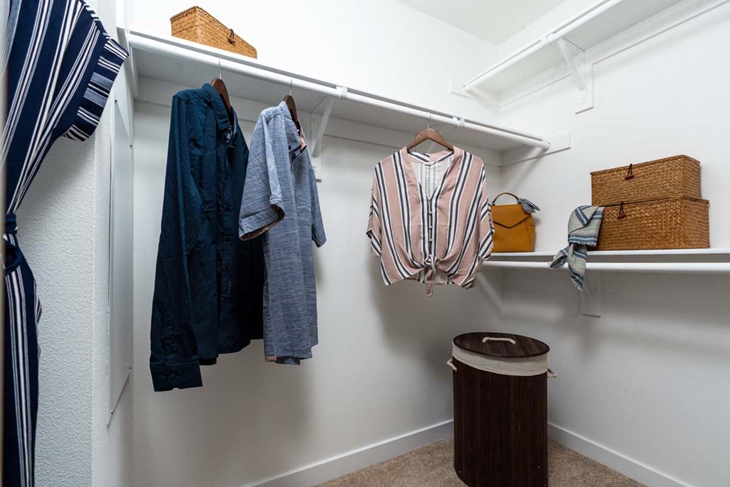 a walk in closet with clothes hanging on the wall and a trash can