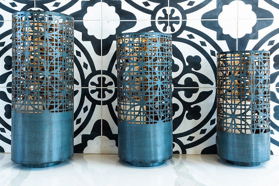 three blue cylinder vases in front of a black and white wallpaper