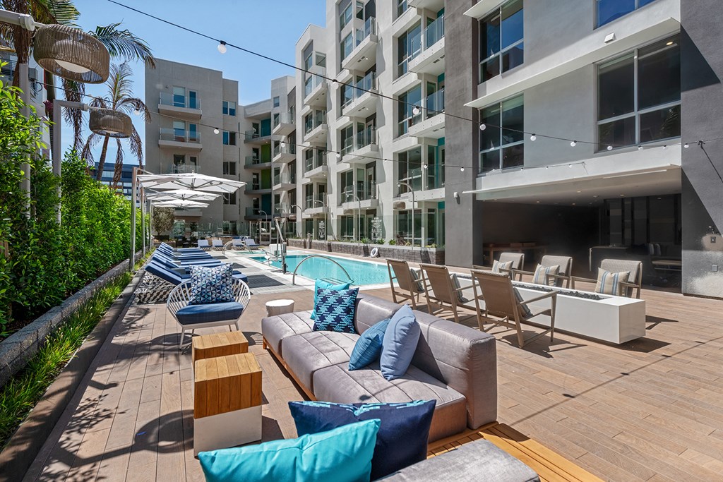 a patio with couches and chairs and a pool in front of an apartment building