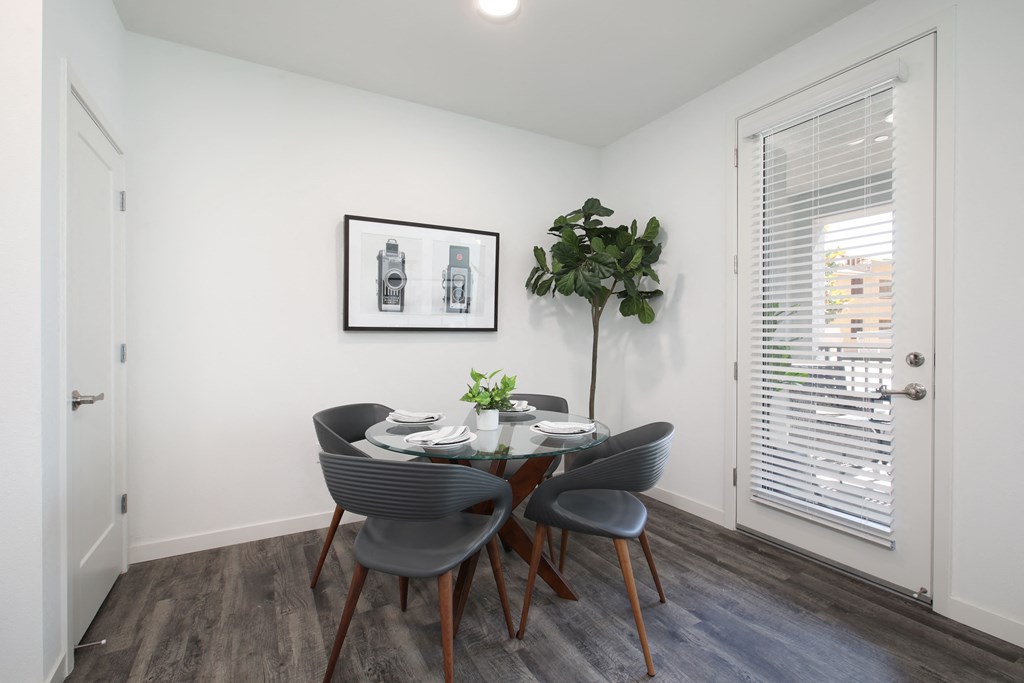 A dining room with a table set for two and a potted plant on the side.
