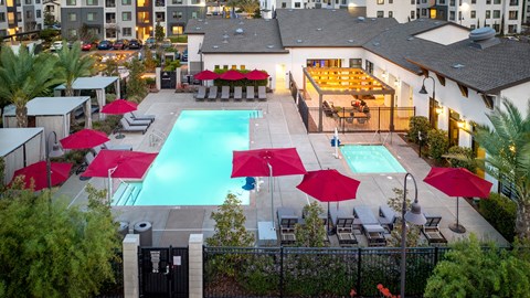 A pool surrounded by red umbrellas and chairs.