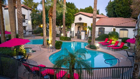 Apartments for Rent Surprise, AZ - The Village at West Point - A Swimming Pool With Palm Trees, Pink Lounge Chairs, And Umbrellas.