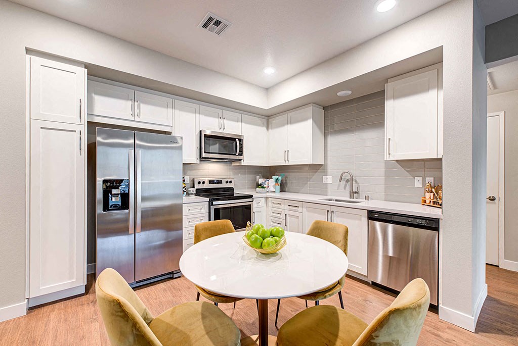 Redlands, CA, Apartments - The Summit - Kitchen With Contemporary Plank Flooring, Quartz Countertops, Whirlpool Appliances, Hartmark Fine Wood Designer Cabinetry, Round Table With Green Chairs, and Gray Tile Backsplash