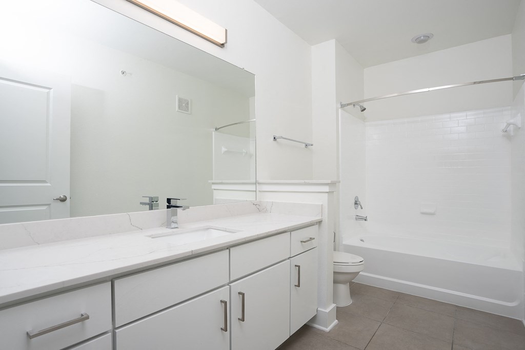 a bathroom with white cabinets and a white toilet next to a white bathtub with a shower at Trend Design District, Texas