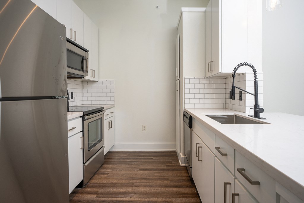 Kitchen with Faux-Wood Flooring, Stainless Steel Appliances, White Cabinetry, White Tile Backsplash, and Quartz Countertops. at Trend Design District, Texas 75207