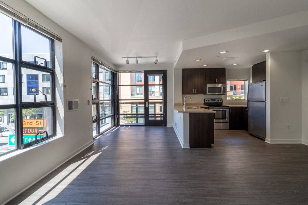 A spacious kitchen and living room with dark wood floors and white walls.