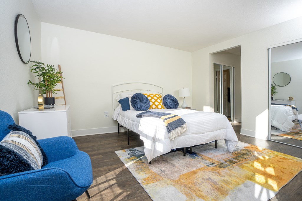 Bedroom wtih bed, blue chair, a large rug and mirror on the wall