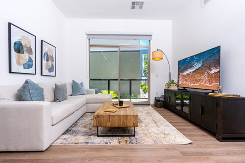 A living room with a white couch, a wooden coffee table, and a large screen TV.