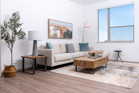 A living room with a couch, a table, a lamp, a plant, and a painting on the wall.