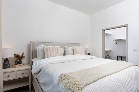 A white bedroom with a large bed and a mirror on the wall.