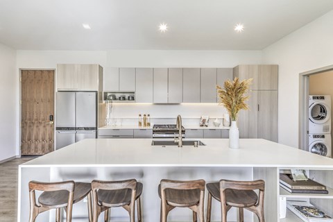 A modern kitchen with a white island and wooden chairs.