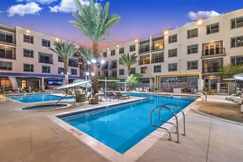 A swimming pool surrounded by palm trees and lounge chairs in front of a building.