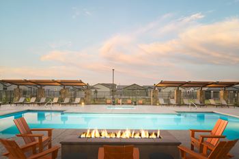 A pool with a fire pit in the middle surrounded by chairs.