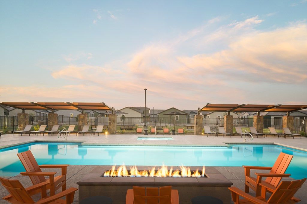 A pool with a fire pit in the middle surrounded by chairs.