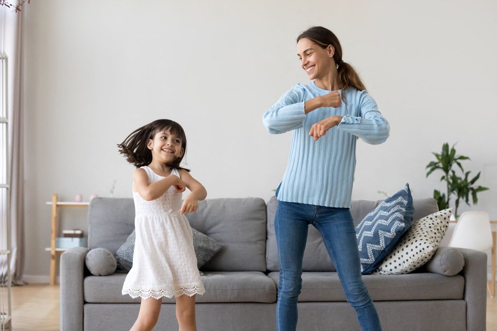 mother and daughter dancing in living room in front of couch