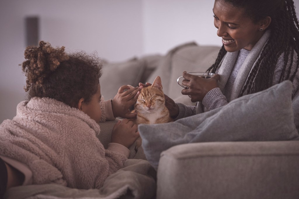 mother and daughter at home petting cat on couch