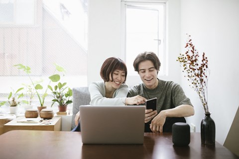 A man and woman are sitting at a table with a laptop and a smartphone.