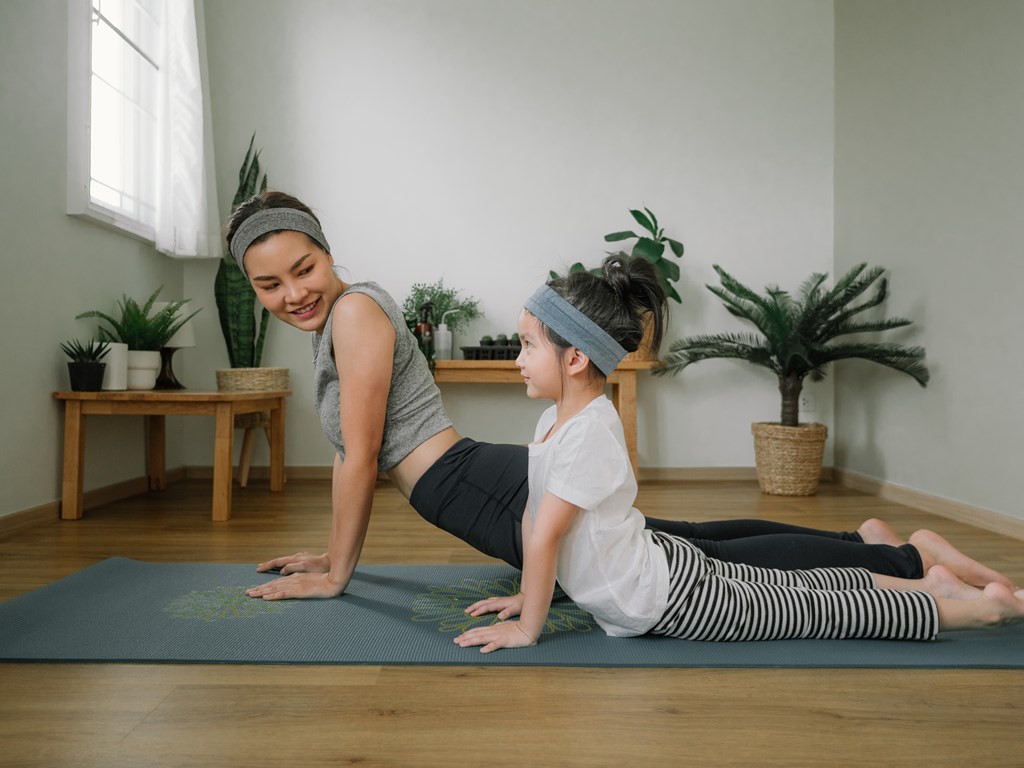Two women doing yoga in a room with plants.