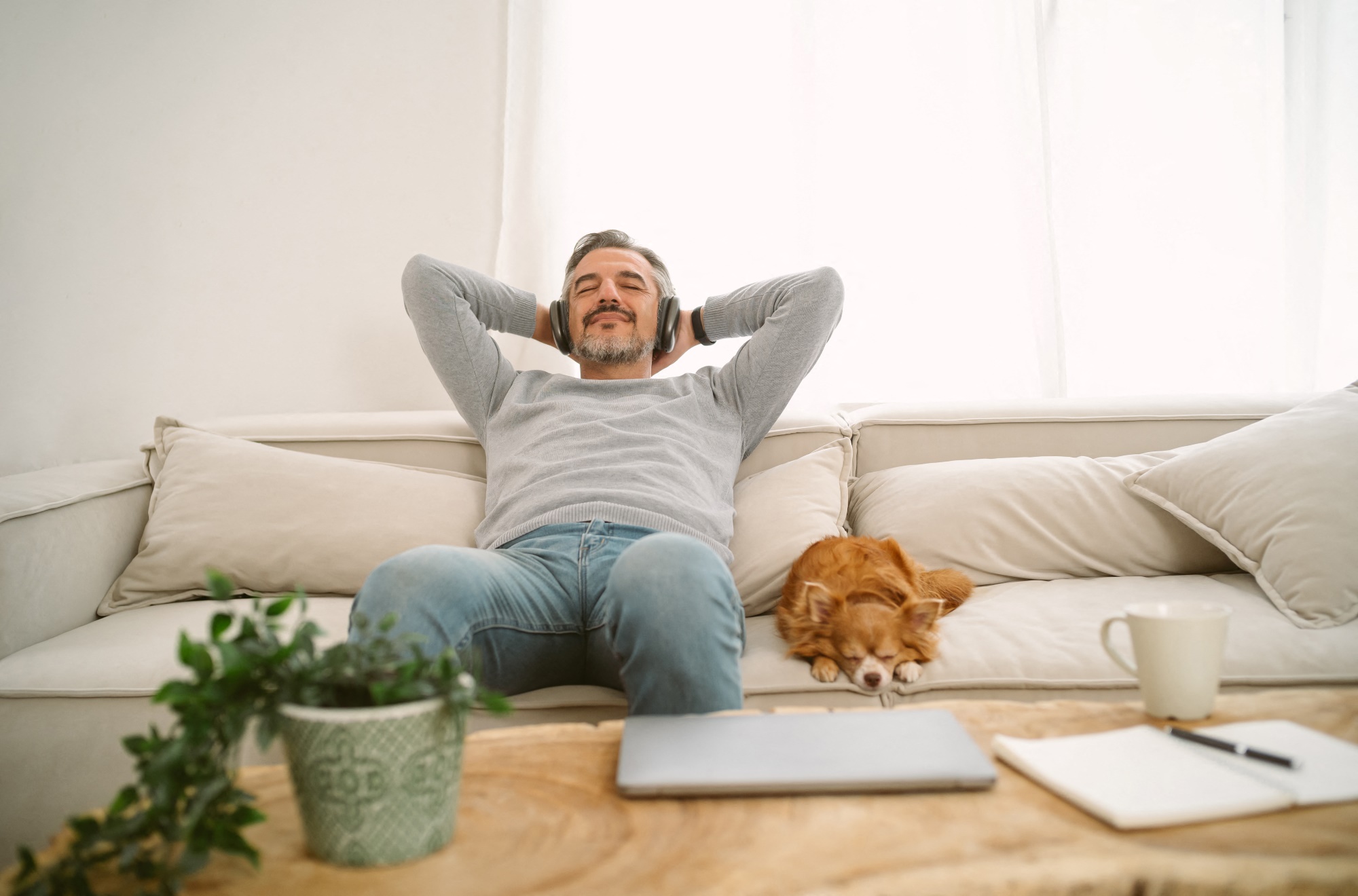 man on couch with dog listening to music on headphones