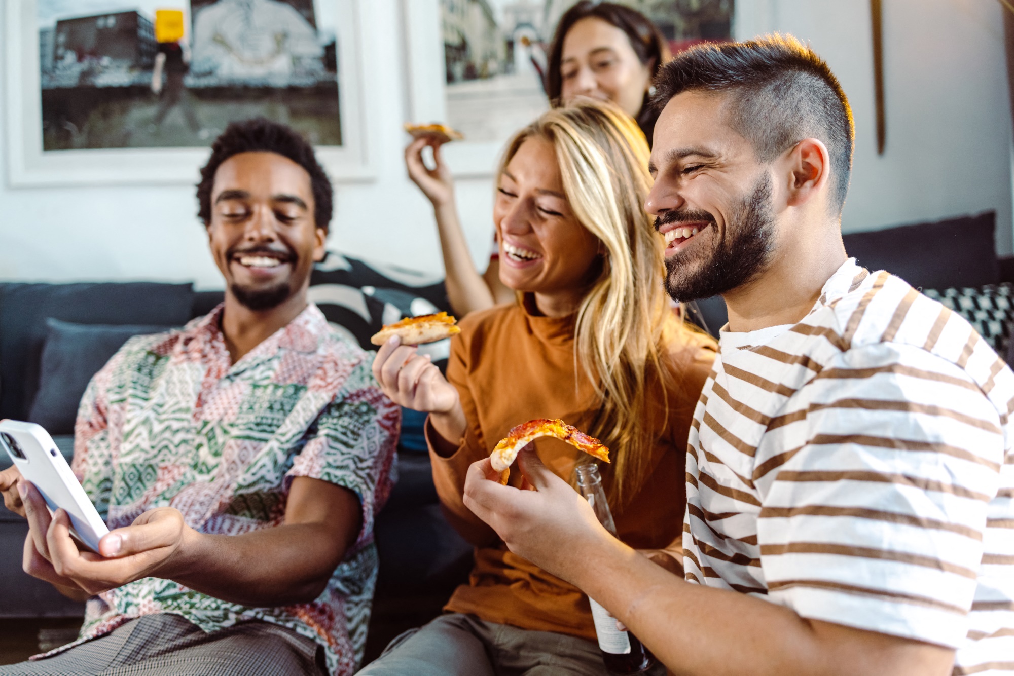 four friends eating pizza at home looking at phone