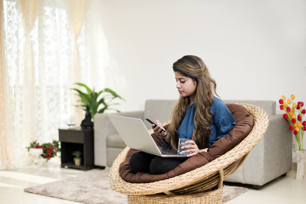 young woman sitting in a bean bag chair using her laptop and texting on her phone