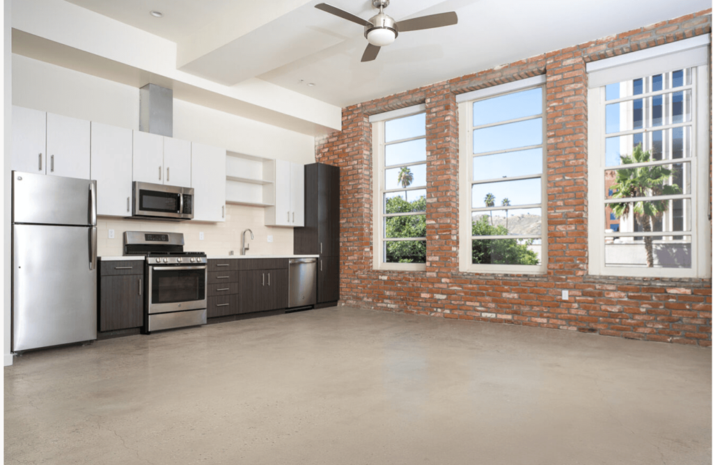 apartment unit kitchen with stainless steel appliances and a brick wall with large windows.