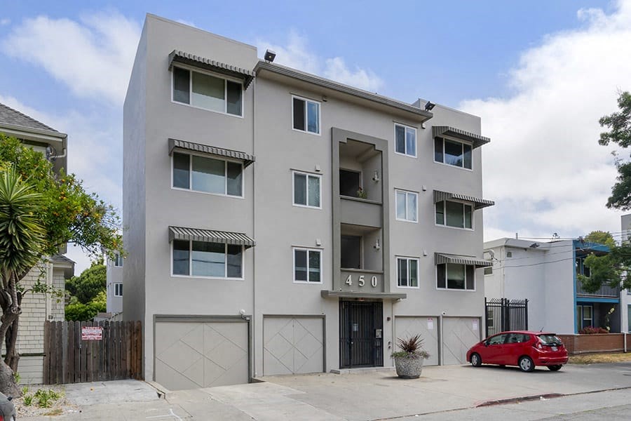 a white apartment building with a red car parked in front of it