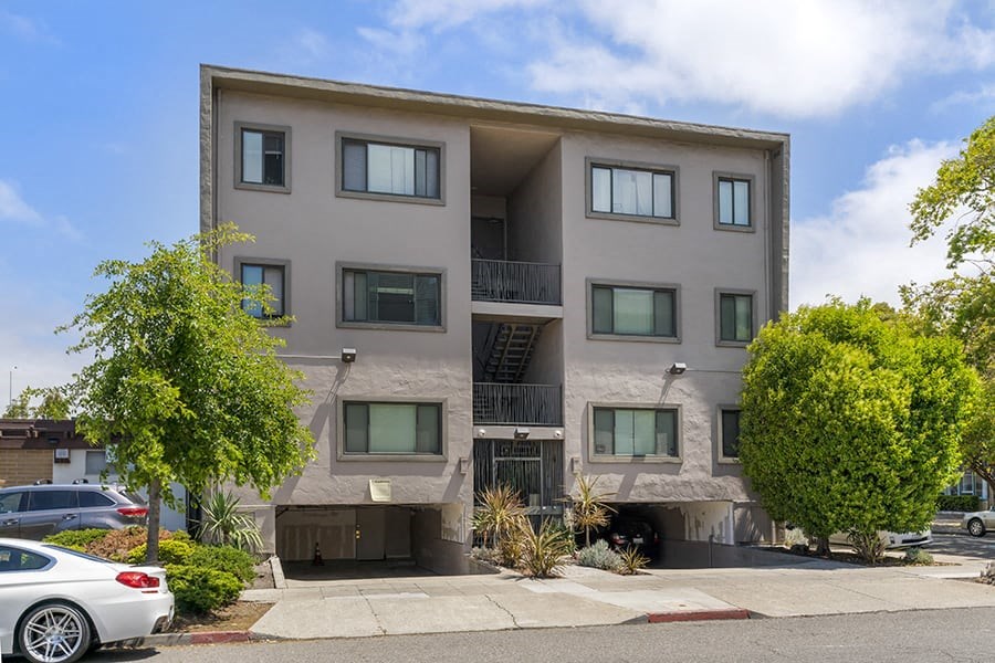 an apartment building with a parking lot and trees in front of it