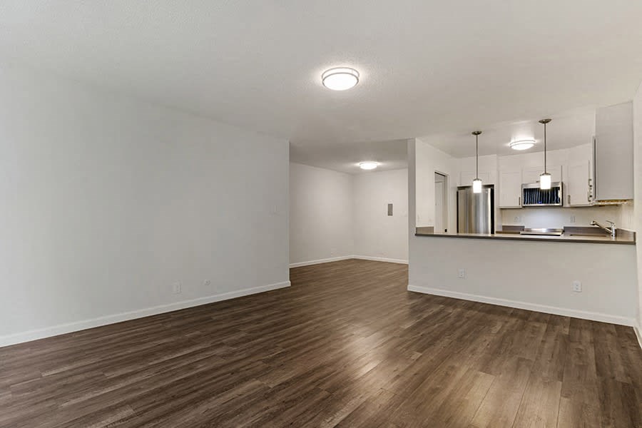 an empty living room with a kitchen in the background