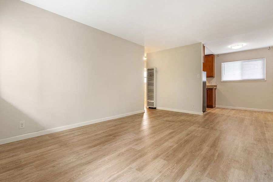 a living room with a wooden floor and a kitchen in the background